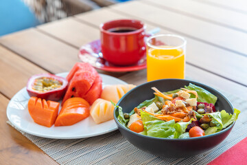 Breakfast. Vegetable salad, fruits such as watermelon, papaya, melon, passion fruit, orange juice and coffee. placed on a gray placemat.