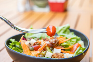 Use a fork a tomato skewer in the foreground and a salad in the background. Breakfast salad with sauteed vegetables on a wooden table