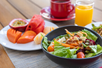 Breakfast. Vegetable salad, fruits such as watermelon, papaya, melon, passion fruit, orange juice and coffee. placed on a gray placemat.