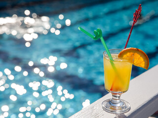 Glass of non alcoholic yellow juice Conga cocktail on pool nosing at tropical resort. Horizontal, cocktail on right side. Healthy cold fresh drink. Pool cocktail party. Copy space