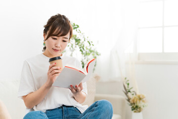 家のソファでホットドリンクを飲む日本人女性（読書）
 - obrazy, fototapety, plakaty