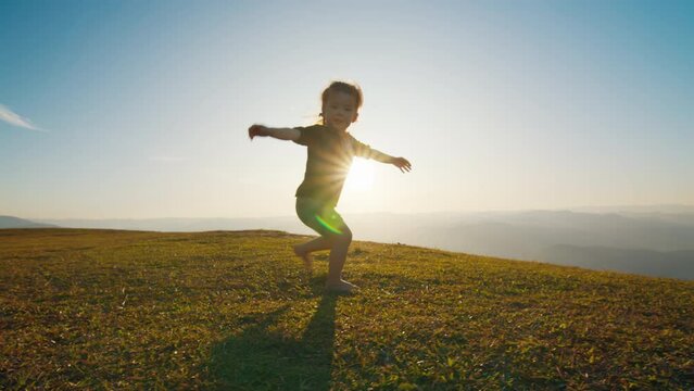 Toddler girl dances and spins around on the grass at sunset