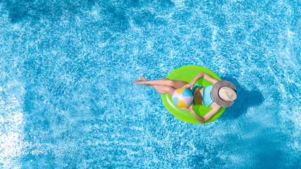 Active young girl in swimming pool aerial drone view from above, teenager relaxes and swims on inflatable ring donut and has fun in water on family vacation, tropical holiday resort
