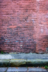 An old brick wall with faded paint with road and rain water gutter in front.