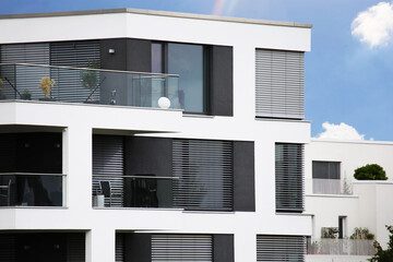 Neues Apartmentgebäude mit weißem Fassadenanstrich und dunklen Jalousien - obrazy, fototapety, plakaty