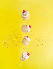 Light berry dessert - cupcakes with air cream and fresh raspberries in a frozen flight on a yellow background with shiny confetti. Sweet food, treat for the holiday. Restaurant, hotel, bakery. - 516506515