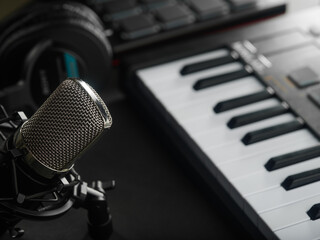 On a dark gray background, a professional synthesizer midi keyboard, studio headphones and a studio microphone. The concept is a recording studio. Recording songs, music albums.