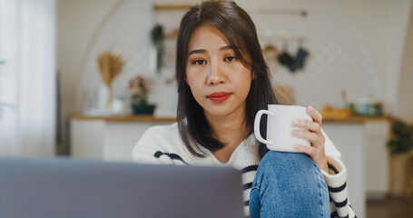Freelance Asia lady casual wear using laptop and drink coffee in kitchen at house. Working from...