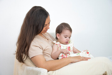 Mom and daughter sit on the background of a white wall smiling