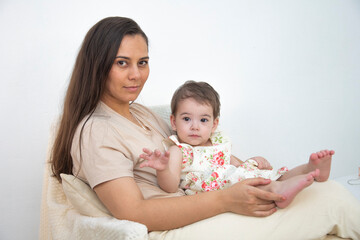 Mom and daughter sit on the background of a white wall smiling
