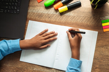 African-american preteen girl doing homework,making notes in notebook at home at her desk.Close up, top view.Back to school concept.School distance education,home schooling,diverse people.