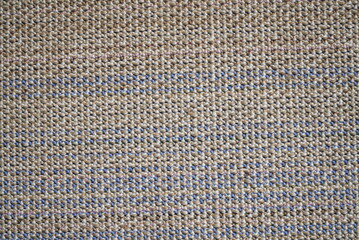 The reverse side of a multi-colored rug, which is a canvas with a white base and horizontal rows of fluffy wool squares of brown, beige, pink and purple colors.