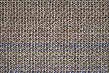 The reverse side of a multi-colored rug, which is a canvas with a white base and horizontal rows of fluffy wool squares of brown, beige, pink and purple colors.