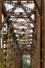 Obraz premium The metal structure of the railway viaduct over the river against the background of a blue sky with clouds.