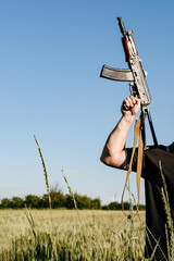 A soldier with a combat military assault rifles AK 74 stands in a field, Ukrainian wheat fields and war.