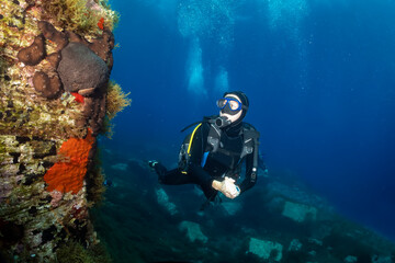 Fototapeta na wymiar A female scuba diver explores a colourful reef in the deep blue of the Aegean Sea in Greece