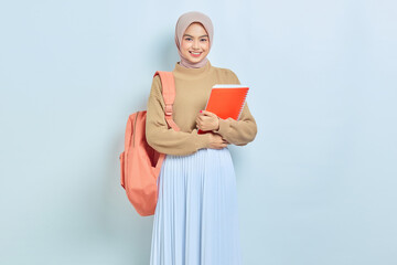 Smiling young Asian Muslim woman student in brown sweater and backpack hold book isolated on white background. back to school concept