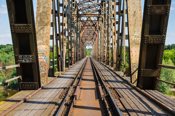The metal structure of the railway viaduct over the river against the background of a blue sky with clouds.