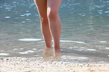 Barefoot woman standing in sea, summer vacation on beach resort. Naked female legs in transparent...