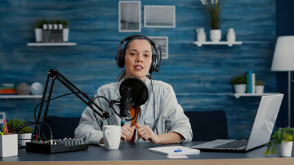 Attractive digital content creator checking microphone while recording daily vlog. Video talk show host speaking to audience about last world events and news while sitting at home studio desk.