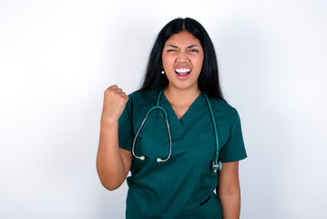 Doctor hispanic woman wearing surgeon uniform over white wall angry and mad raising fist frustrated...