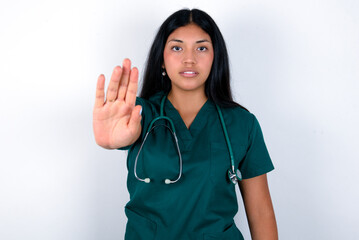 Doctor hispanic woman wearing surgeon uniform over white wall doing stop sing with palm of the...