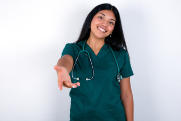 Doctor hispanic woman wearing surgeon uniform over white wall smiling friendly offering handshake as greeting and welcoming. Successful business.