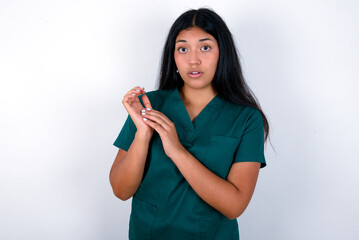 Surprised emotional Doctor hispanic woman wearing surgeon uniform over white wall rubs palms and stares at camera with disbelief