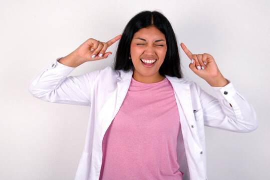 Photo of crazy Young hispanic doctor girl wearing coat over white background screaming and pointing with fingers at hair closed eyes