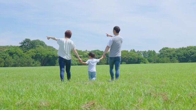 手を繋いで晴天の緑地を歩く親子3人
