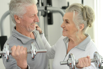 Elderly couple exercising in the gym with dumbbells