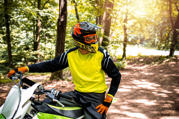 Portrait of professional dirt bike rider preparing for the motocross race through the forest.