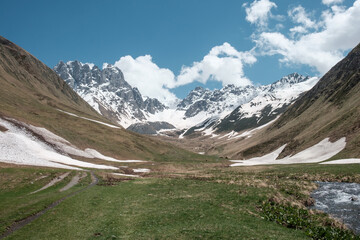 Georgia, Caucasus Mountains, Juta valley - river, snow, blue sky, mountain from stones and snowy peak Chaukhebi in summer.