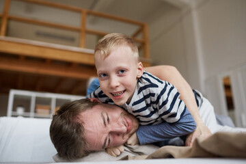 Portrait of cheerful excited boy with blond hair fighting with father playfully while they having fun at home