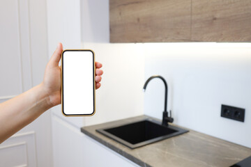 Kitchen background with hand with phone. Blurred home kitchen with blank smartphone screen. Online grocery ordering concept, online food shopping.