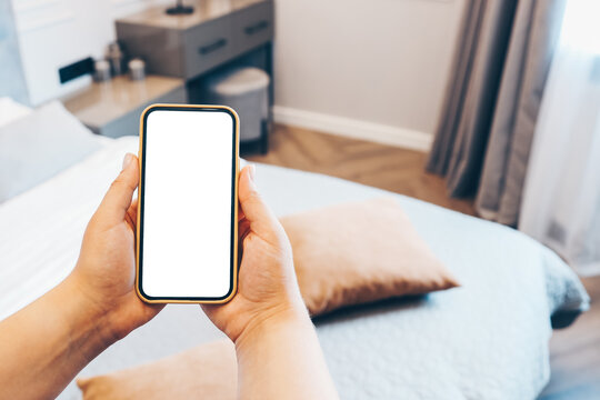 Mockup image of woman's hand holding phone with blank white screen at home