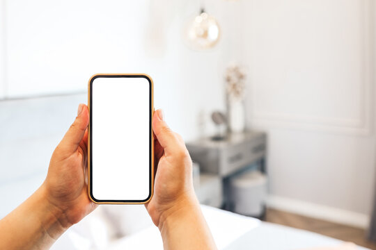 Mockup image of woman's hand holding phone with blank white screen at home