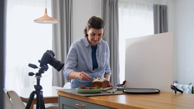 blogging, cooking and people concept - happy smiling female photographer or food blogger with camera and berries decorating cake in kitchen at home