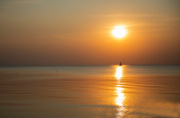 Obraz premium Golden sea and sunset sky with the silhouette of a small sailboat on the horizon