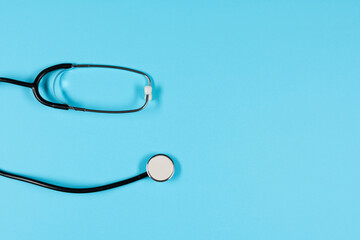 Black stethoscope, top view on  the blue background. Medical equipment, tool for measuring the heart rate, lungs, and abdomen sounds