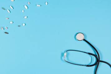 Top view of black stethoscope and colorfull pills scattered all over the blue background.