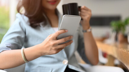 Relaxed female entrepreneur drinking coffee and checking online news or email on her smart phone