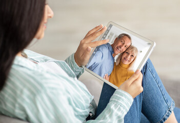 Young Woman Holding Digital Tablet And Making Video Call To Senior Parents