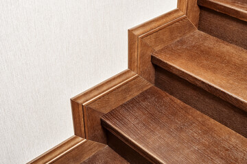 Wooden steps of indoor staircase with stair skirtboard made of toned solid oak and oak veneer close...