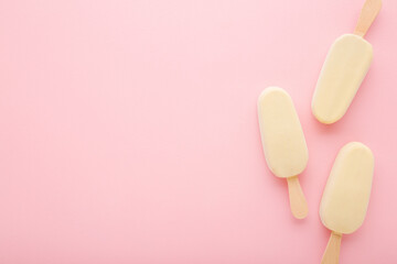 Chocolate ice cream with white vanilla glaze on sticks. Light pink table background. Pastel color. Closeup. Cold sweet snack in summer. Empty place for text. Top down view.