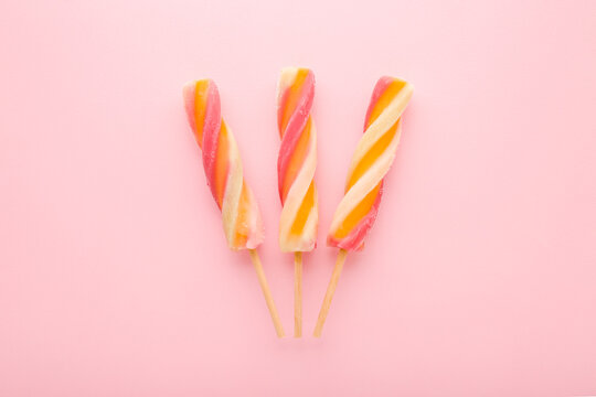 Three colorful fruit ice popsicles on sticks. Light pink table background. Pastel color. Closeup. Cold sweet snack in summer. Top down view.
