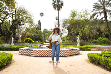 Fototapeta na wymiar Mature and attractive woman, with curly brown hair, wearing a brown leather jacket over her shoulder, shirt and jeans, walking in a happy and independent park. Concept beauty, happiness, empowerment.
