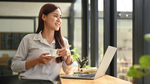 Elegant Asian Woman Entrepreneur Thoughtfully Looking Out The Office Window While Holding Cup Of Coffee In Her Hands