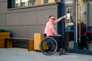 man with disability who uses a wheelchair dials the access code to the apartment on the door of the...