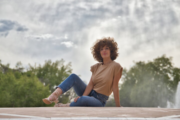 Fototapeta na wymiar Mature and attractive woman, with curly brown hair, brown shirt and jeans, sitting on the floor with a seductive attitude. Concept seduce, beauty, provoke, sensuality, hairstyle.